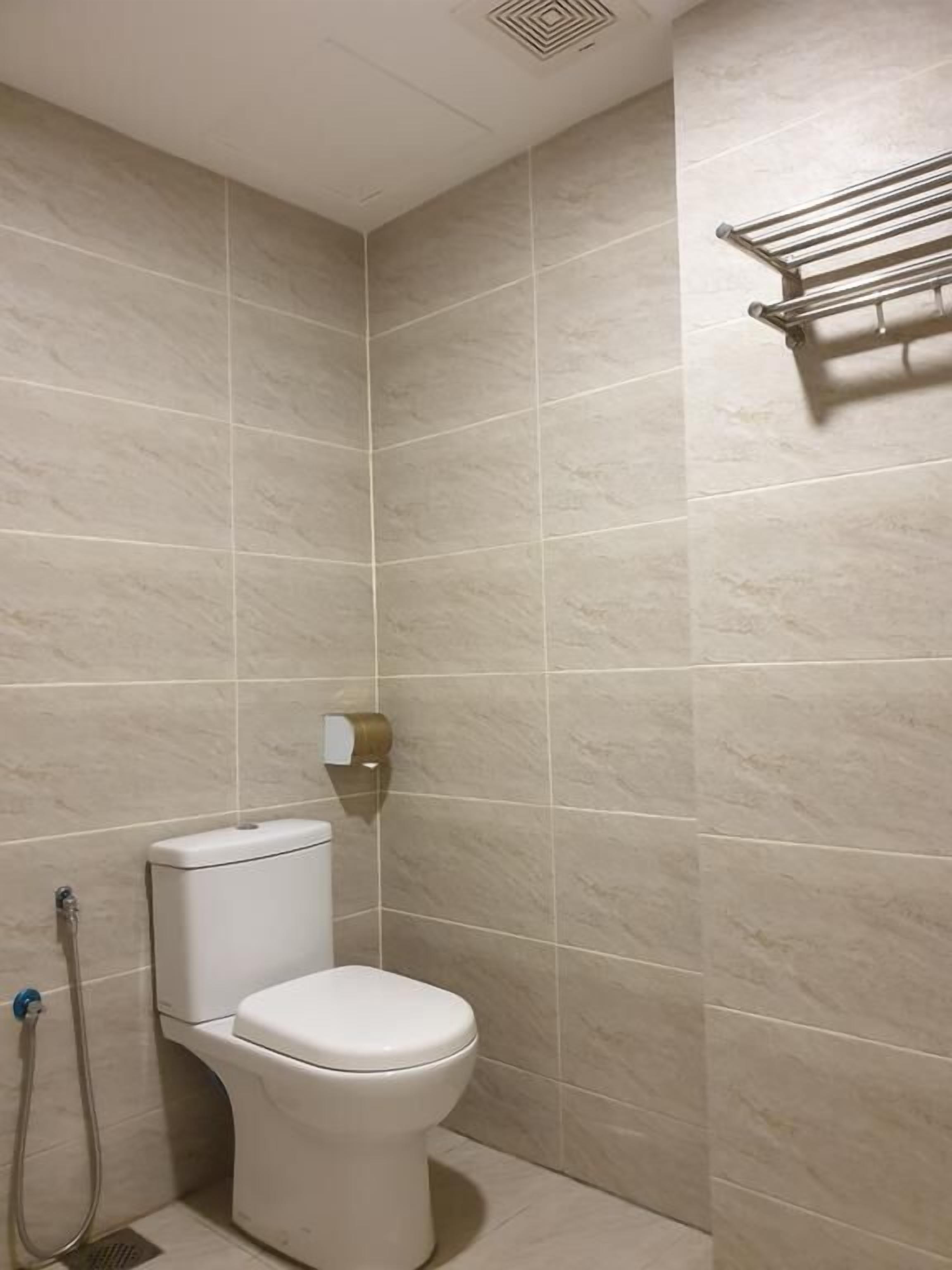 A small, tiled bathroom with a toilet, a towel rack, and a shower hose.