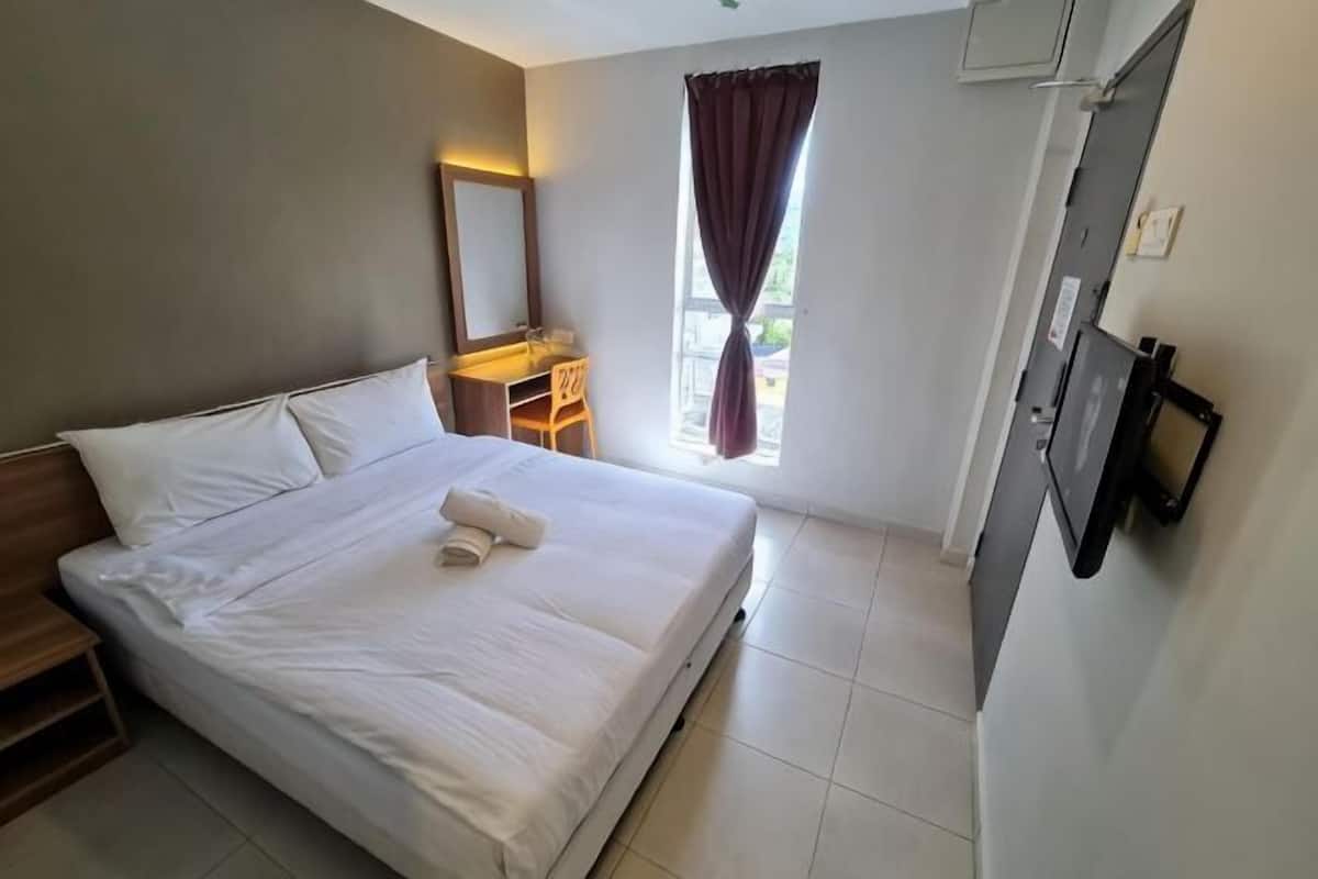 A hotel room with a bed, a desk, a chair, a window with curtains, and a wall-mounted TV.