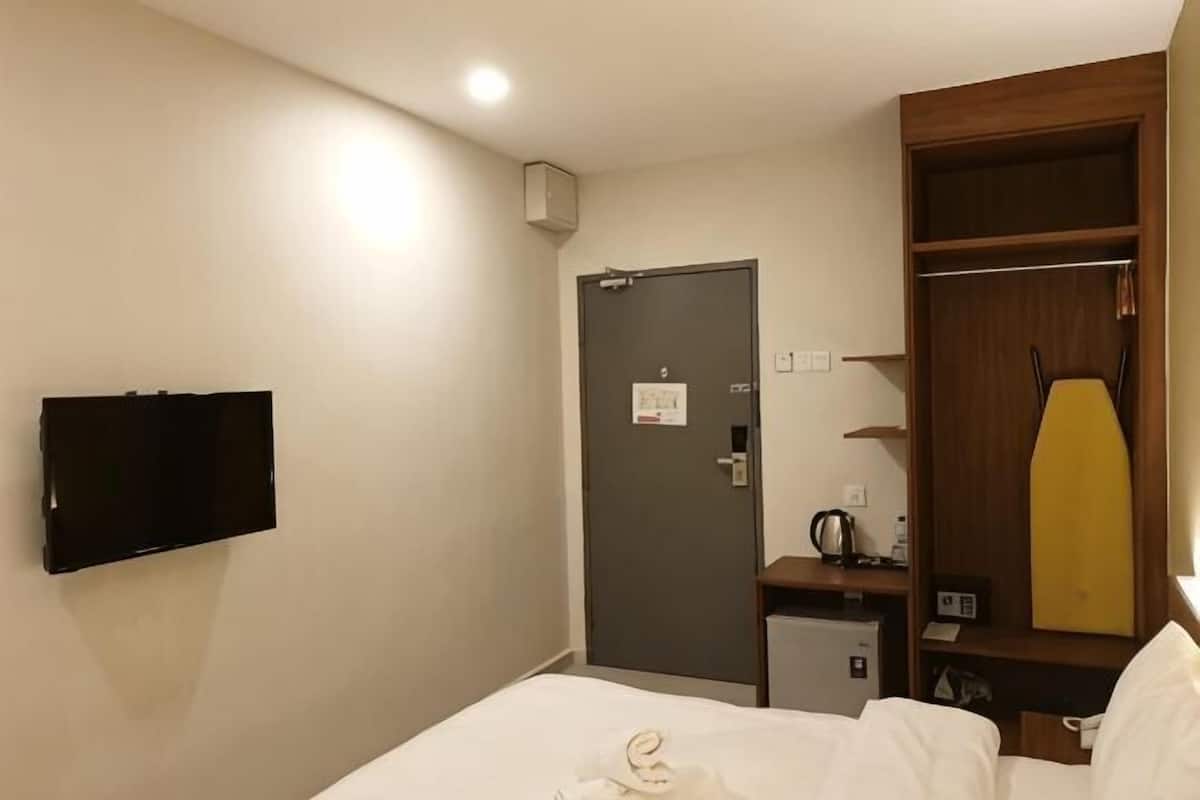 A hotel room with a bed, a television mounted on the wall, a wardrobe, and a desk with a kettle.