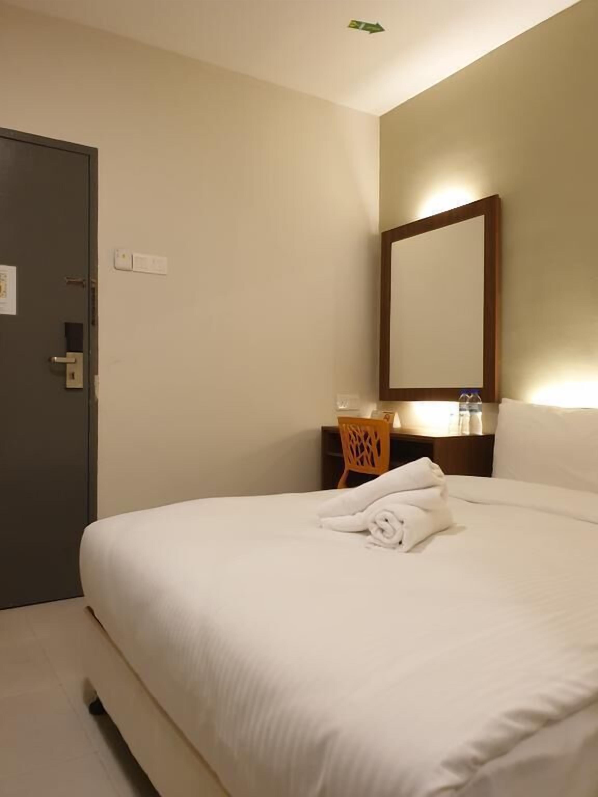 Quarto de hotel com cama, cadeira, mesa de cabeceira, espelho e porta.