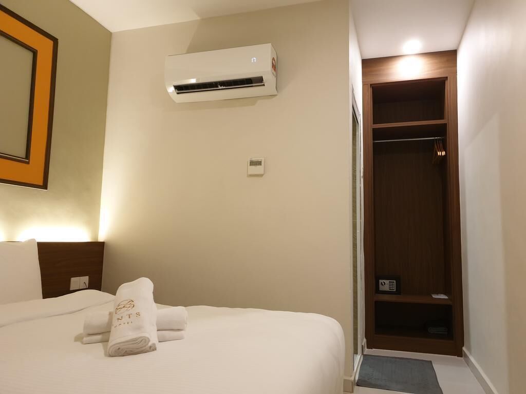 A hotel room with a bed, an air conditioning unit, a wooden wardrobe, and a framed picture on the wall.