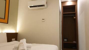 A hotel room with a bed, an air conditioning unit, a wooden wardrobe, and a framed picture on the wall.