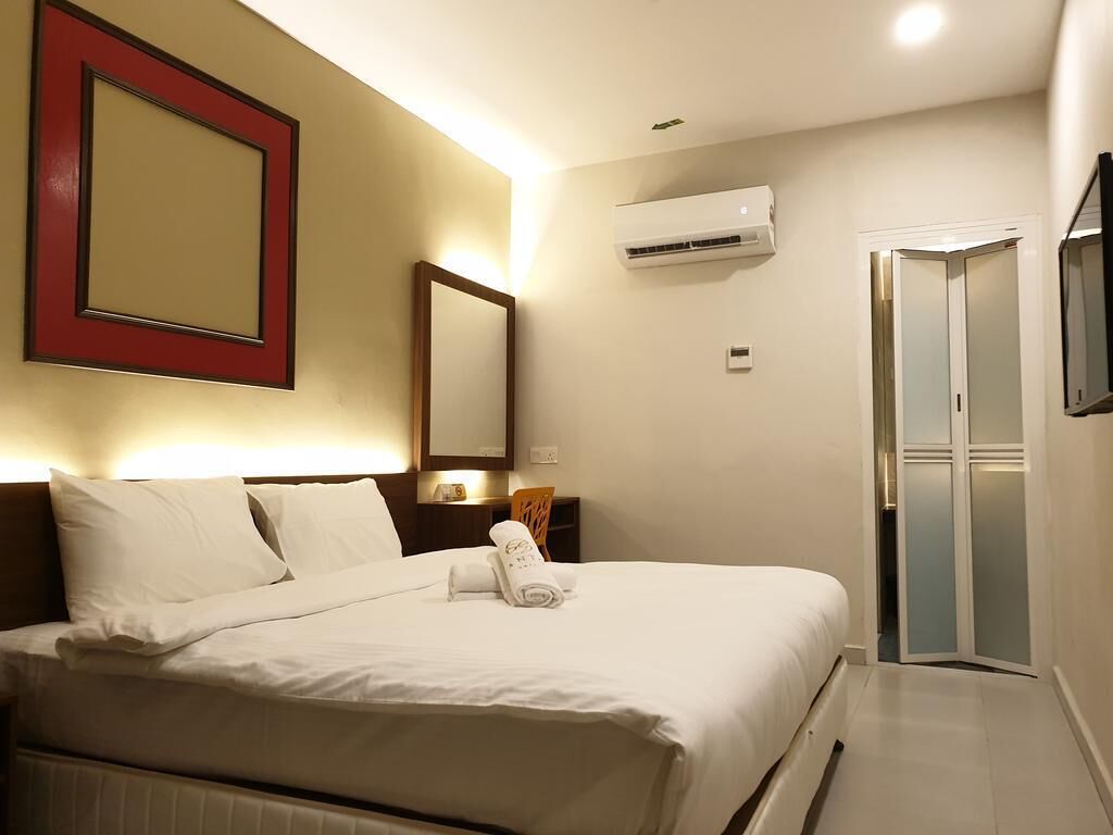 A hotel room with a bed, a bedside table, an air conditioning unit, a mirror, and a sliding door.