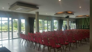 A conference room with rows of red chairs, large windows, and a view of the outdoors. - Ants Hotel (Kangar)