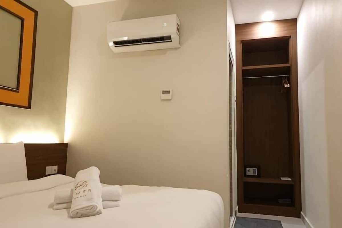 A hotel room with a bed, an air conditioning unit, a wooden closet, and a mirror on the wall.