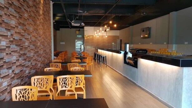 A modern restaurant with a brick wall, wooden chairs, a long counter, and pendant lighting. - Ants Hotel (Kangar)