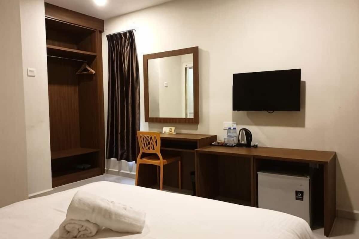A hotel room with a bed, a desk, a chair, a wardrobe, a television, and a small refrigerator.