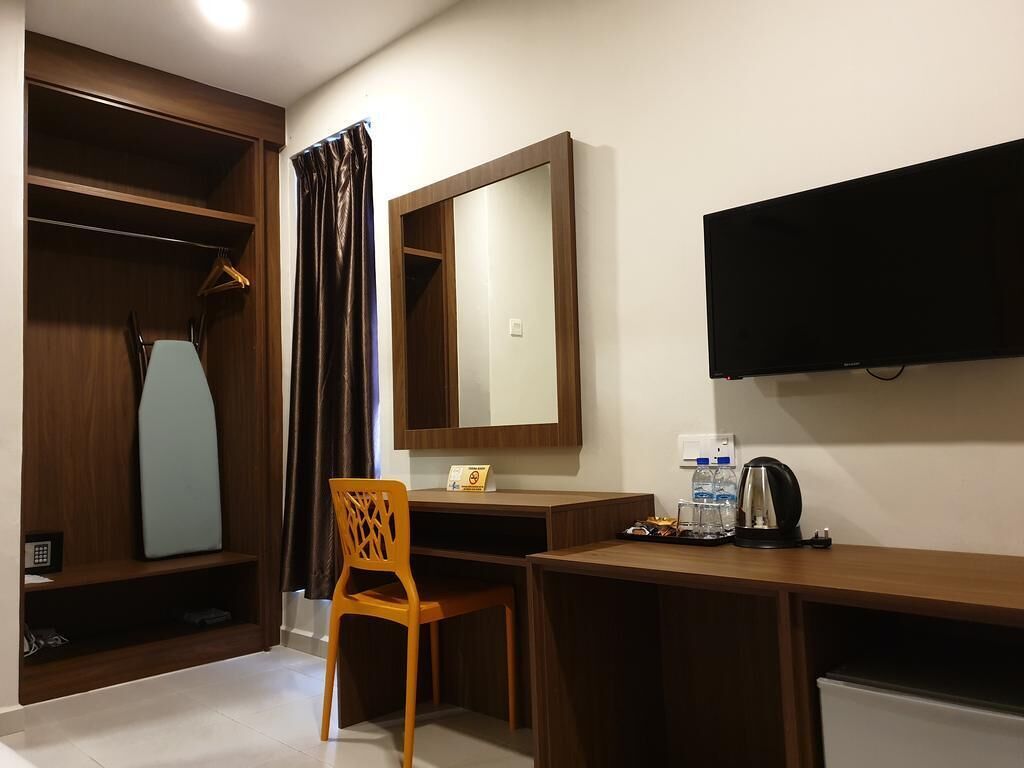 A hotel room with a wooden desk, a chair, a television, a mirror, and a wardrobe.