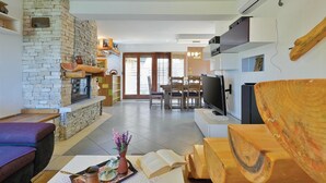 Ein modernes Wohnzimmer mit Kamin aus Stein, einem Essbereich mit Fernseher und einer Küchenzeile mit Geräten.