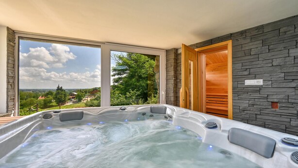 Ein Whirlpool mit Steinwand und Holztür, große Fenster mit Blick auf Grünflächen und Gebäude.