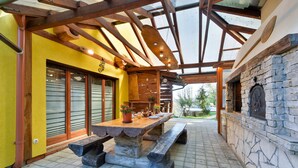 Eine Terrasse im Freien mit Steintisch und Bänken, einem Backofen aus Ziegeln und einer gelben Wand mit Schiebetüren.