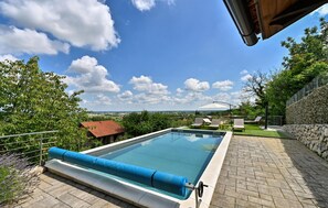 Relax by the serene pool surrounded by lush greenery and a clear sky.