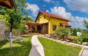 Charming home surrounded by lush greenery, featuring a wooden porch and a stone wall.