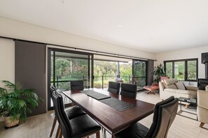 A modern interior with a dining area, a sofa, and a large sliding glass door leading to a balcony. - Waterside One | Secluded Luxury (Margaret River)