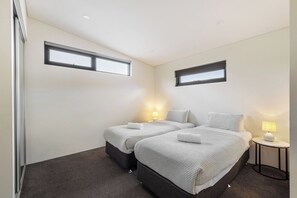 Een slaapkamer met twee bedden, een klein nachtkastje met een lamp en een raam.