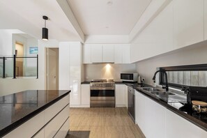 A modern kitchen with white cabinetry, a stainless steel range, a microwave, and a black countertop. - Waterside One | Secluded Luxury (Margaret River)
