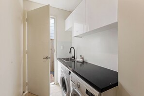 A compact laundry area with a washing machine, a sink, and a countertop. - Waterside One | Secluded Luxury (Margaret River)