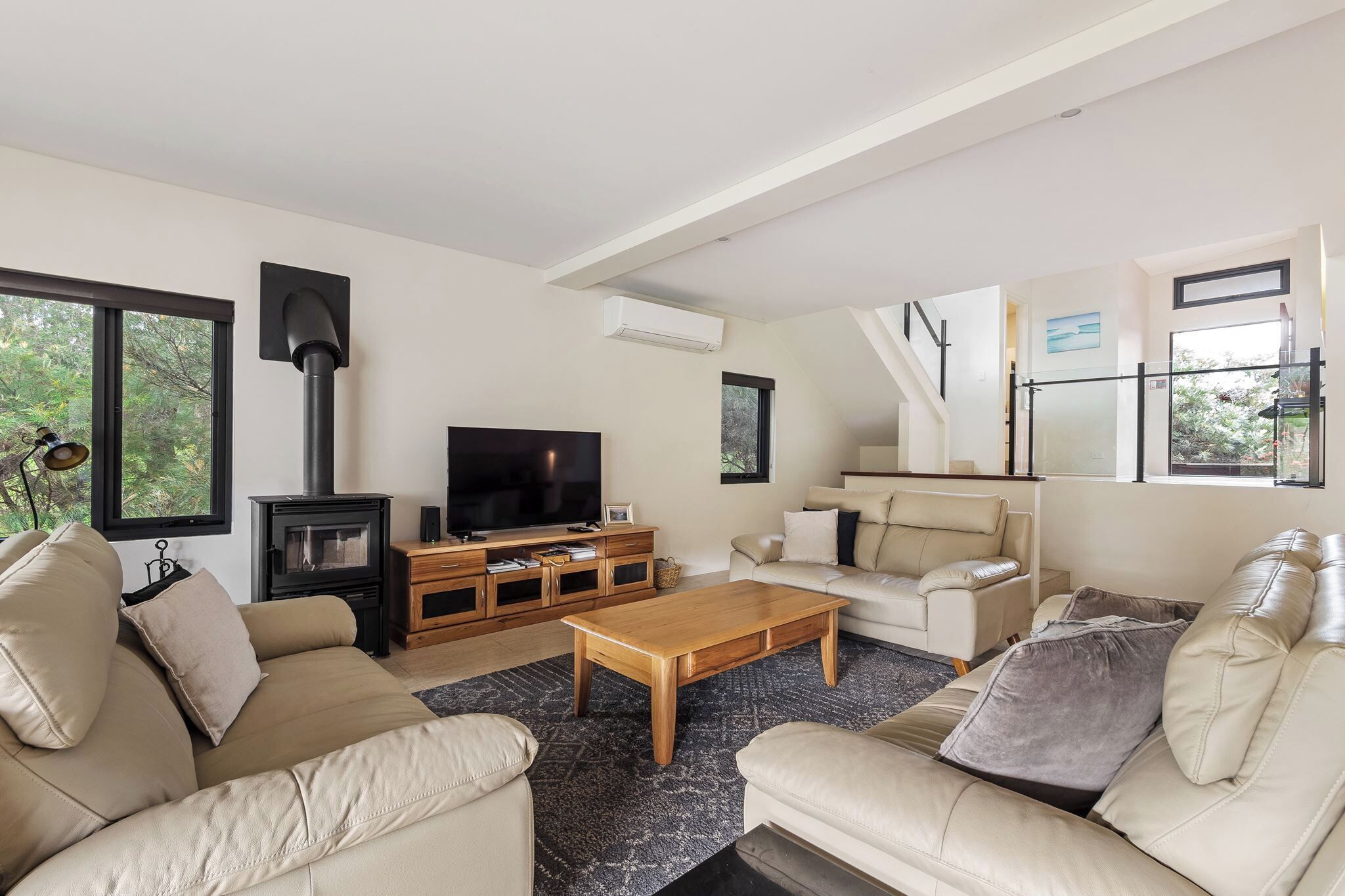 A modern living room with a fireplace, sofa, coffee table, TV, and a staircase leading to a balcony.