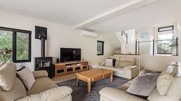 A modern living room with a fireplace, sofa, coffee table, TV, and a staircase leading to a balcony.