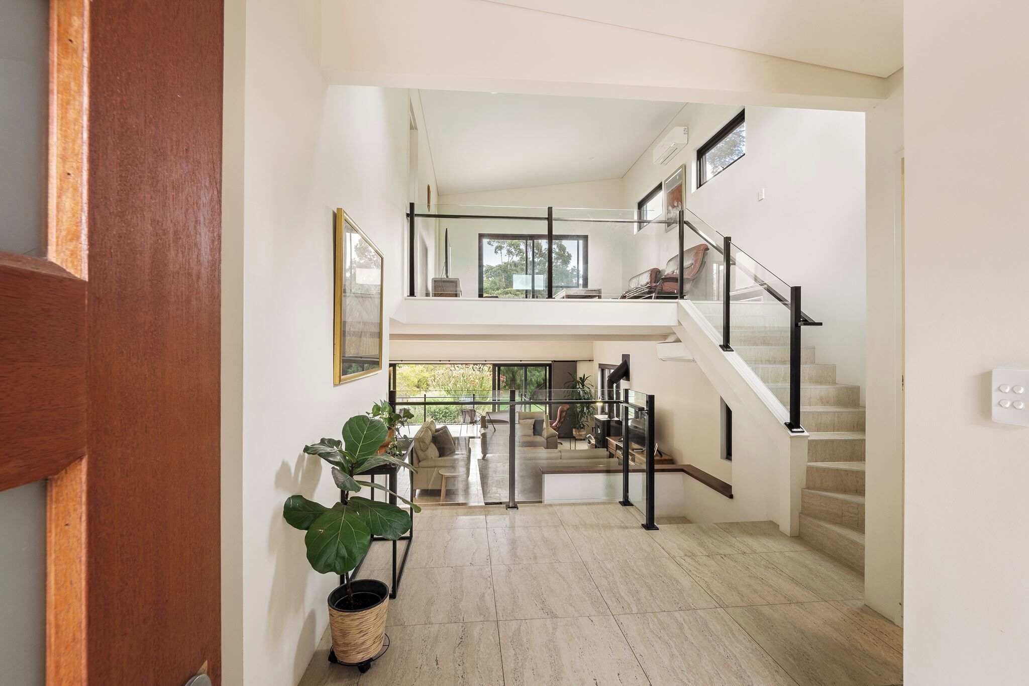 Un intérieur spacieux avec un escalier menant à un niveau supérieur, un coin salon offrant une vue sur l’extérieur et une plante en pot.