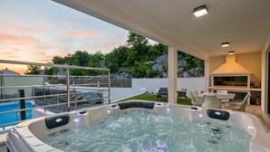 Ein Whirlpool mit Blick auf einen Swimmingpool und eine Terrasse mit Gartenmöbeln.