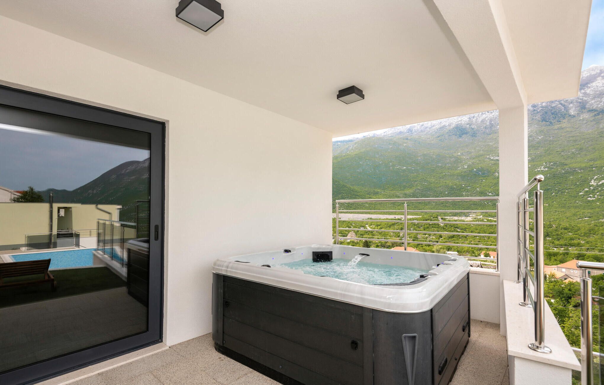 A balcony with a hot tub, a pool, and a mountain view.