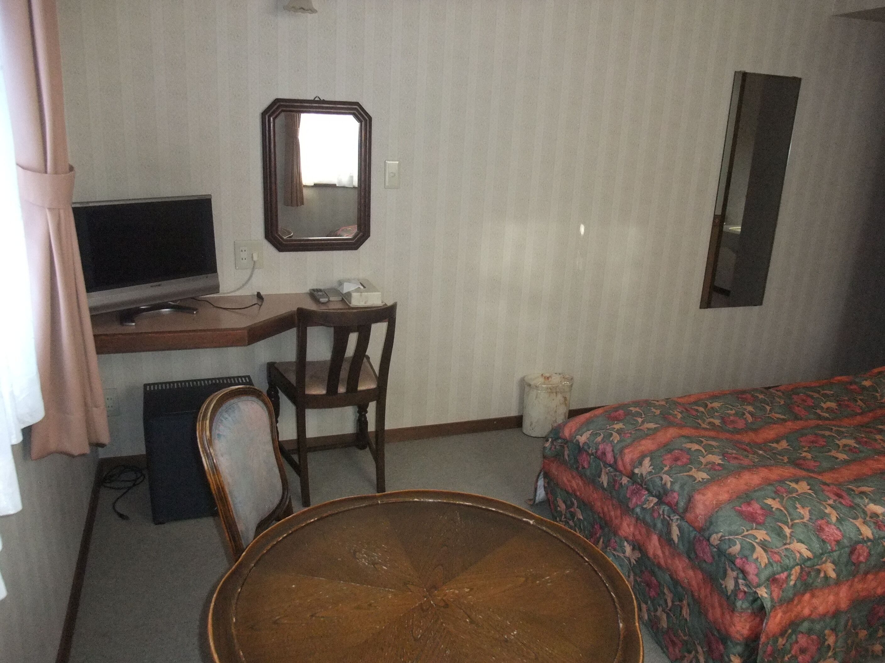 A hotel room with a desk, chair, bed, and a large mirror.