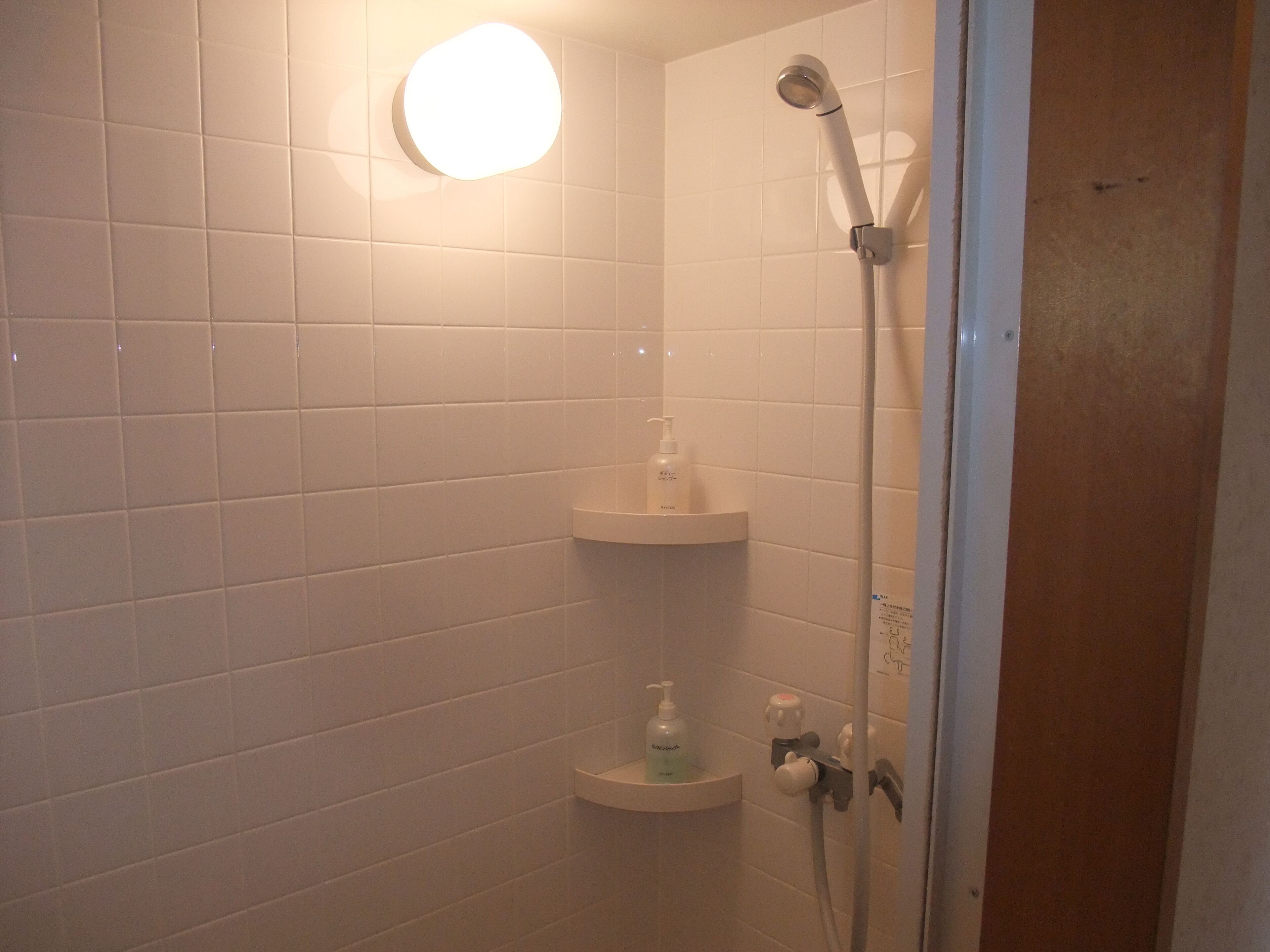 A bathroom with white tiled walls, a shower with a handheld showerhead, and two shelves with toiletries.
