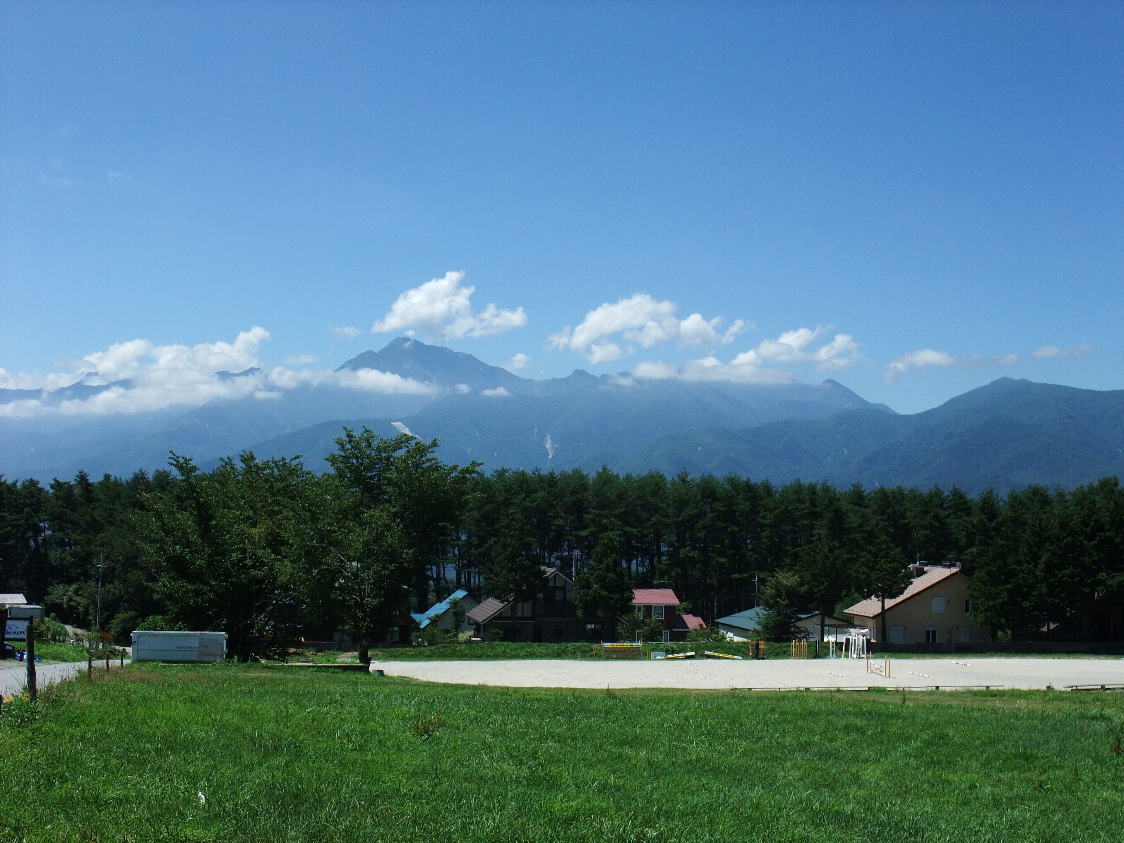 A grassy field with a clear view of distant mountains and a few buildings in the foreground.