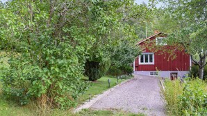 A red house with a gravel driveway and a garden path leading to it.