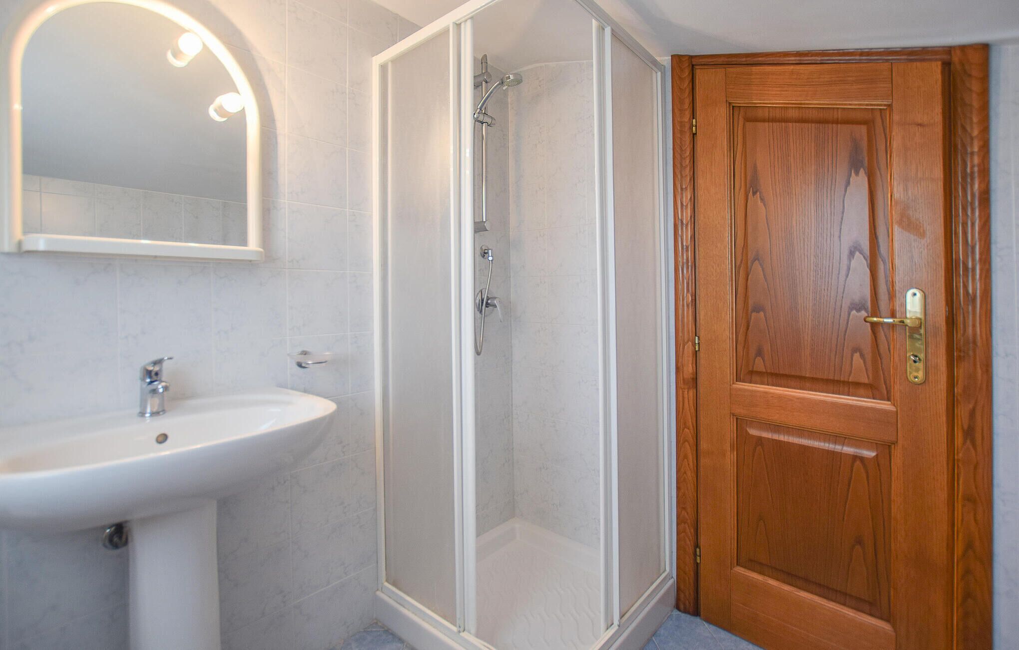 A bathroom with a white sink, a glass-enclosed shower, and a wooden door.