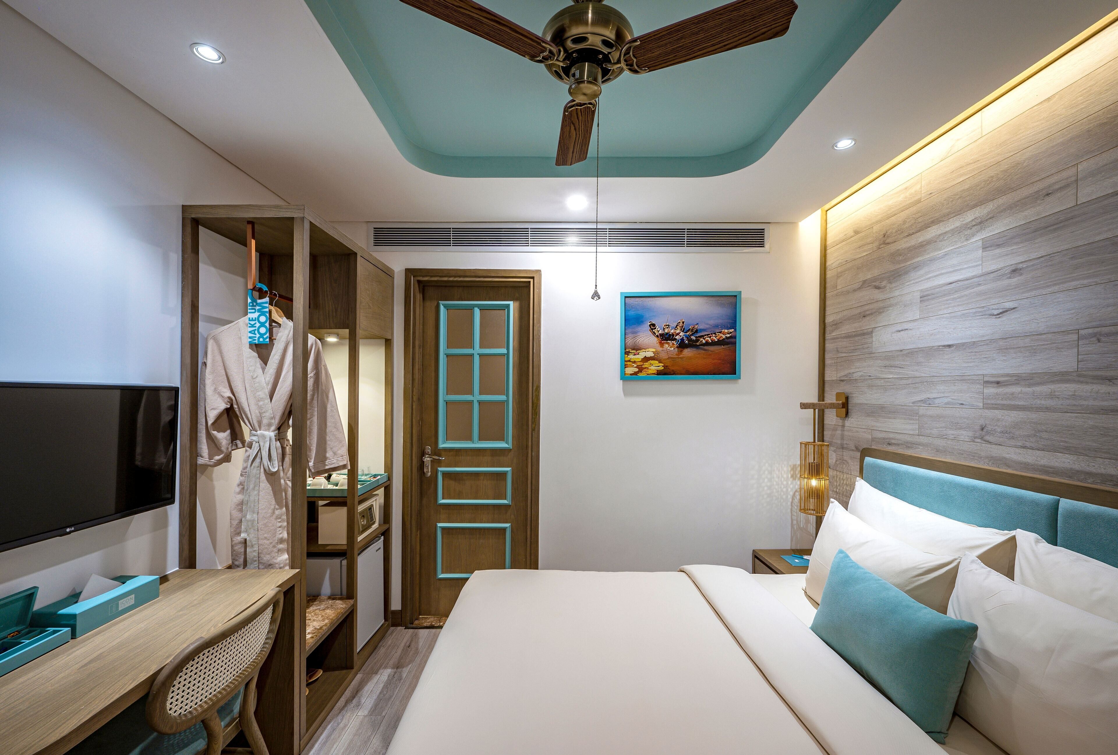 A hotel room with a bed, a desk, a TV, a robe, and a wooden headboard.