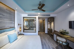 Une chambre d’hôtel moderne dotée d’un grand lit, d’un bureau avec une chaise, d’un ventilateur de plafond et d’un téléviseur fixé au mur.