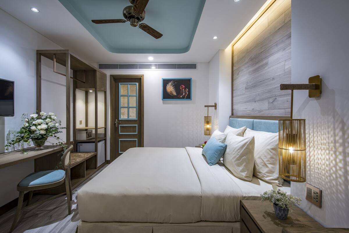 A bedroom with a bed, bedside table, lamp, chair, desk, and a ceiling fan.