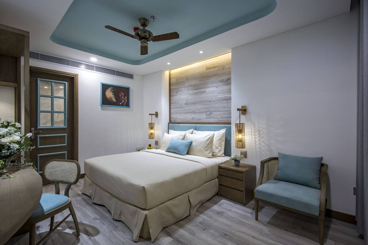A bedroom with a bed, bedside tables, a chair, a ceiling fan, and a wall-mounted light fixture.