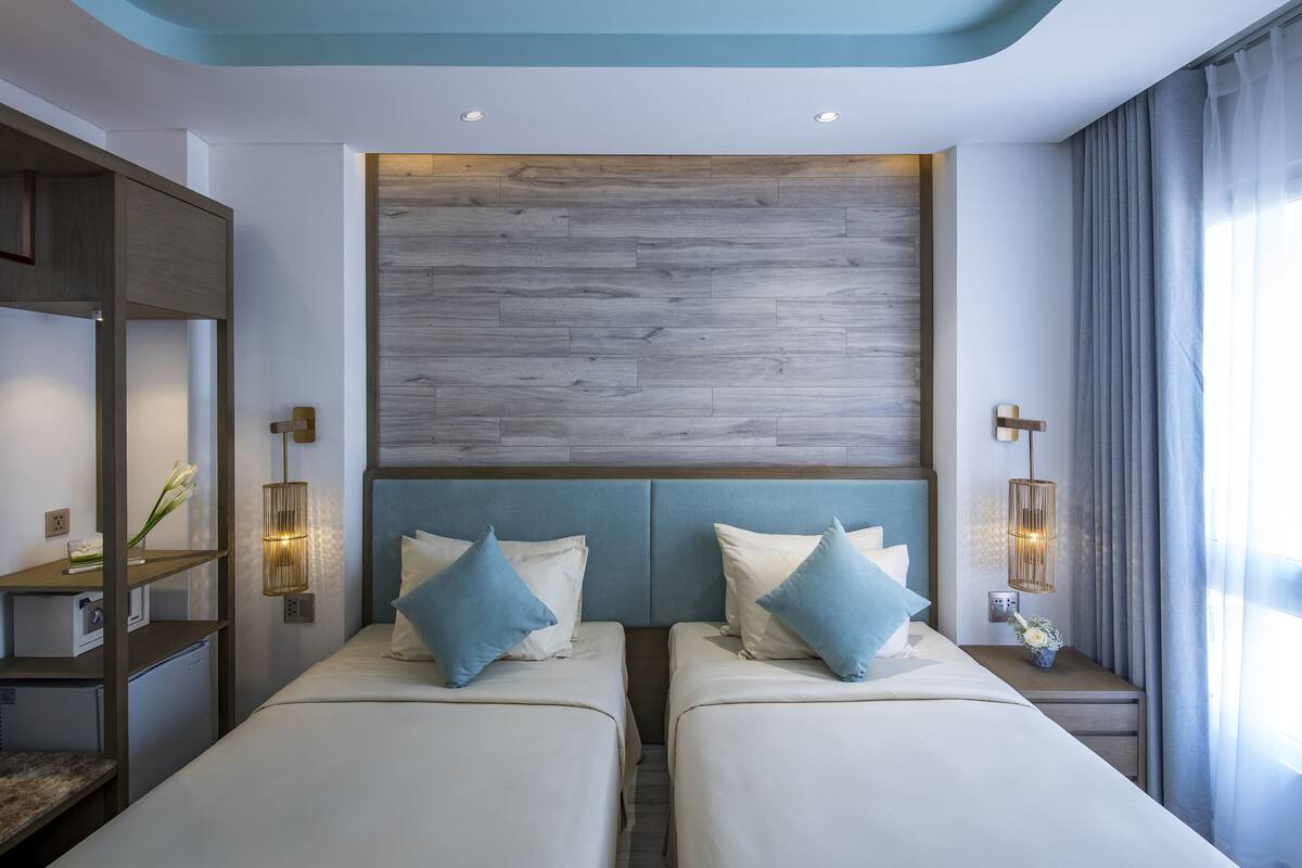 A hotel room with two beds, a wooden headboard, bedside lamps, and a nightstand with a vase.