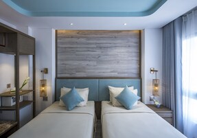 A hotel room with two beds, a wooden headboard, bedside lamps, and a nightstand with a vase.
