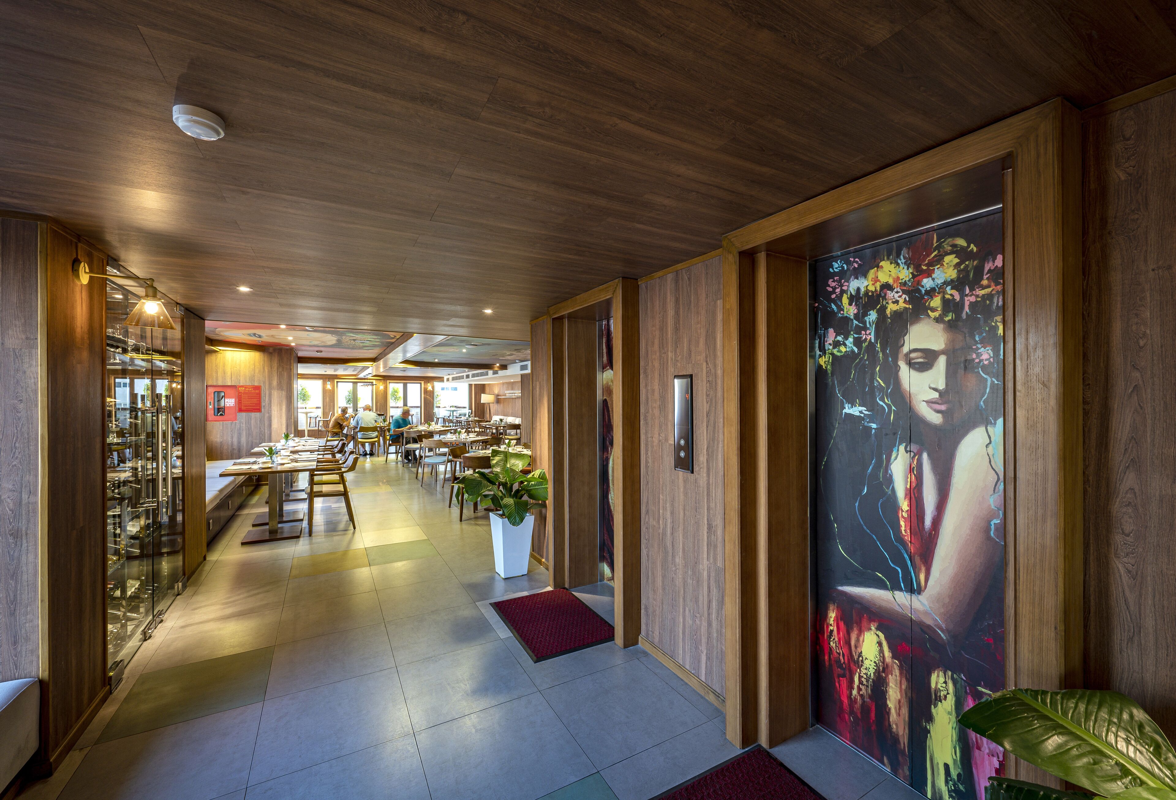 Ein Hotelkorridor mit Holzwänden, einem großen Blumenbild und einer Sitzecke mit Tischen und Stühlen.