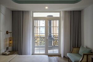 A hotel room with a bed, a bedside table with a phone, a chair, and a balcony with curtains.