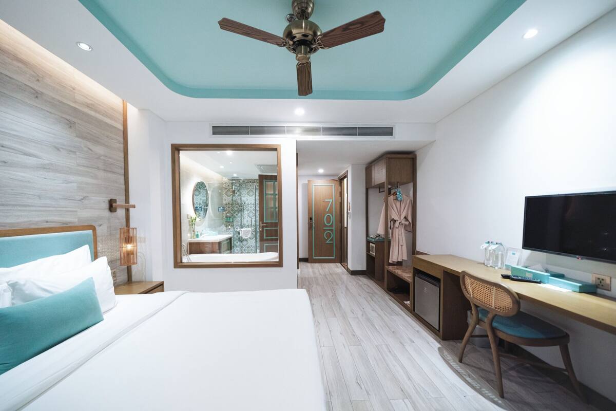 A modern hotel room with a bed, desk, chair, TV, and a ceiling fan.