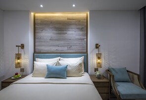 A modern bedroom with a wooden headboard, a bed with white and blue bedding, two bedside tables with lamps, and a small side table with a vase.