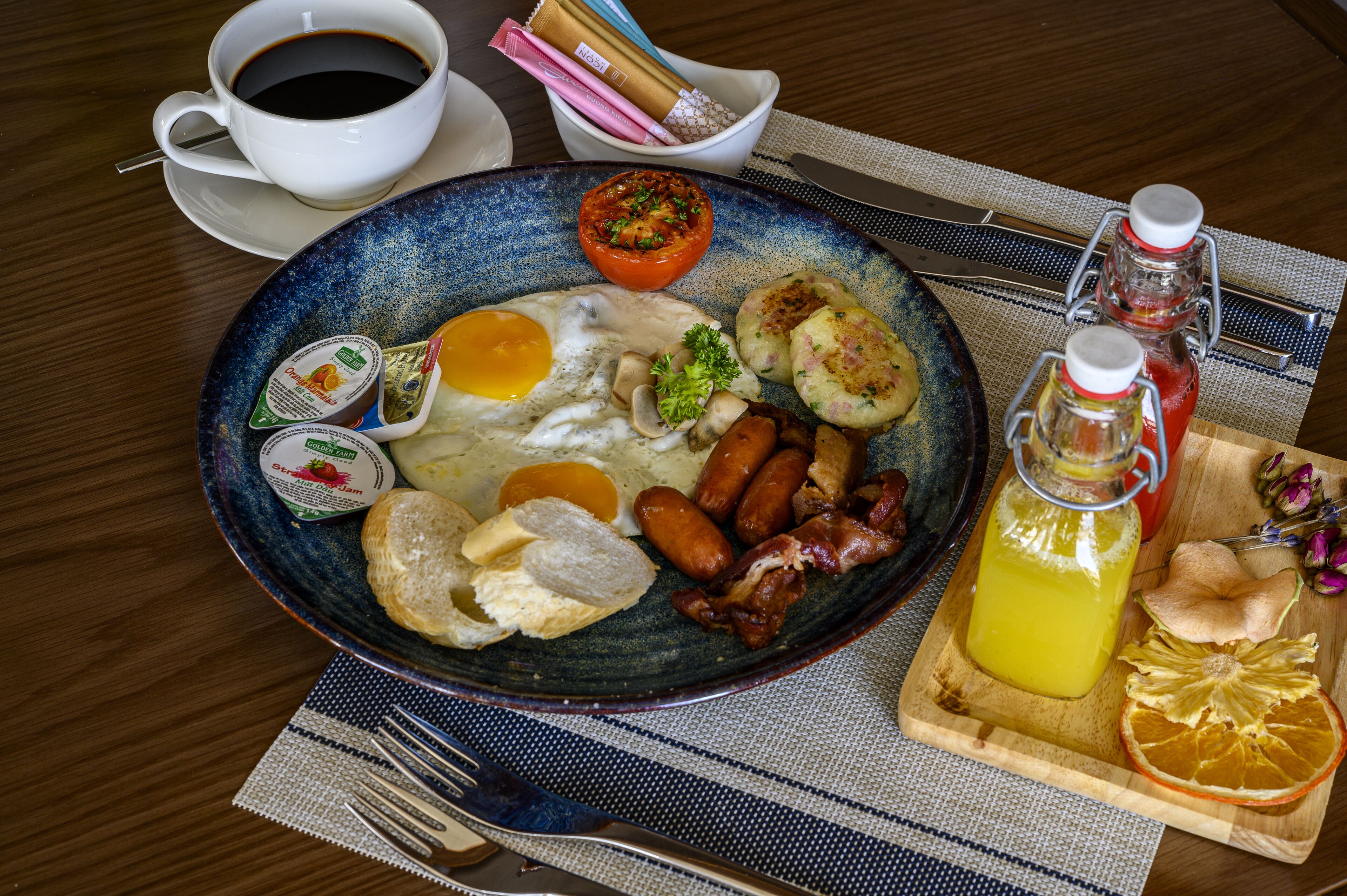 A breakfast plate with eggs, sausages, bacon, and toast, accompanied by a cup of coffee and condiments.