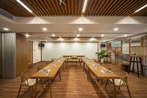 Un salón de conferencias con una larga mesa de madera, sillas y una pantalla para proyector.