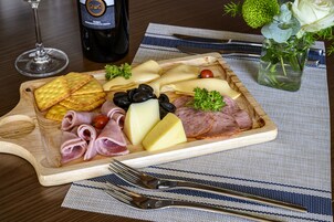 Pöydällä on puinen tarjoilulauta, jonka päällä on erilaisia juustoja, leikkeleitä ja keksejä.