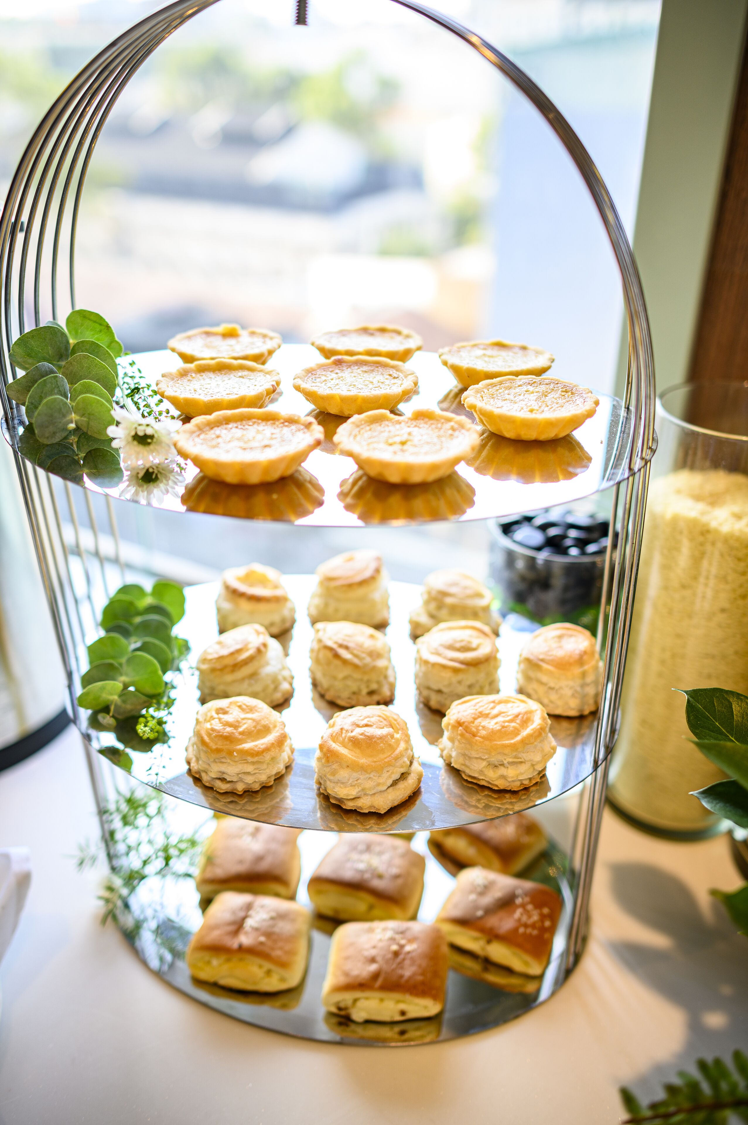 A tiered dessert display with various pastries, including scones and tarts, on a reflective stand.