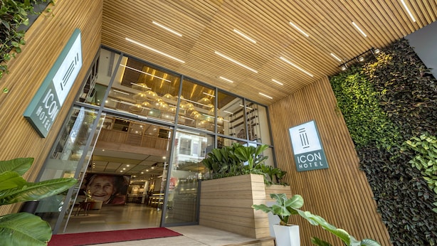 Exterior del ICON Hotel con un diseño moderno, destacando una fachada de madera, un amplio acceso de vidrio y plantas de interior.