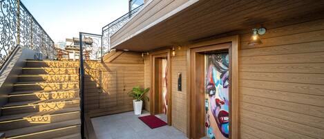 Un bâtiment moderne avec un revêtement mural en bois, un escalier dont les marches sont illuminées et une porte ornée d’une fresque colorée.