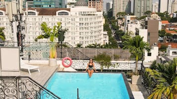 Una piscina en la azotea con vistas a la ciudad, rodeada de edificios y palmeras.