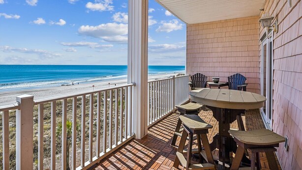 A covered outdoor area with a view of the beach, a table with chairs, and a railing. - Atlantis Villas 202 by Elliott Beach Rentals (NORTH MYRTLE BEACH)