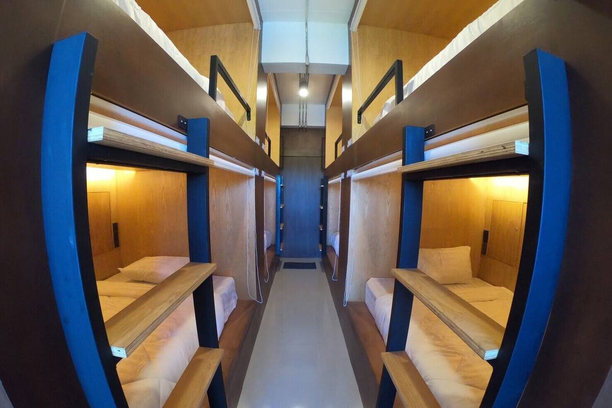 A narrow corridor with bunk beds on either side, wooden walls, and overhead lighting.